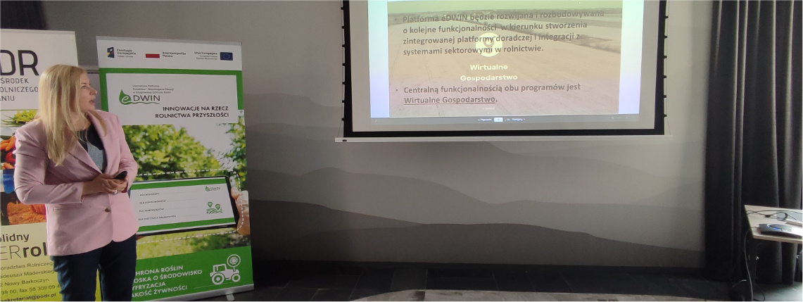 Anna Pietruczuk z Centrum Doradztwa Rolniczego w Brwinowie opowiadała o dalszych perspektywach rozwoju platformy doradczej eDWIN Młoda kobieta - Anna Pietruczuk - w różowej marynarce stoi i wygłasza prezentację. Za nią widać dwa rollupy. Kobieta patrzy się na rzutnik, na którym wyświetlona jest prezentacja o platformie eDWIN.