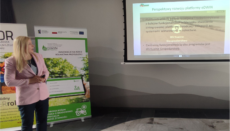 Anna Pietruczuk z Centrum Doradztwa Rolniczego w Brwinowie opowiadała o dalszych perspektywach rozwoju platformy doradczej eDWIN Młoda kobieta - Anna Pietruczuk - w różowej marynarce stoi i wygłasza prezentację. Za nią widać dwa rollupy. Kobieta patrzy się na rzutnik, na którym wyświetlona jest prezentacja o platformie eDWIN.