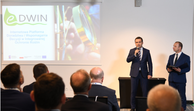 Otwarcia konferencji dokonał Jacek Sommerfeld, dyrektor Wielkopolskiego Ośrodka Doradztwa Rolniczego w Poznaniu Wnętrze sali wykładowej. Dyrektor WODR Jacek Sommerfeld stoi w z mikrofonem w ręku. Obok niego stoi moderator konferencji. Przed mężczyznami widoczni są od tyłu słuchacze konferencji.