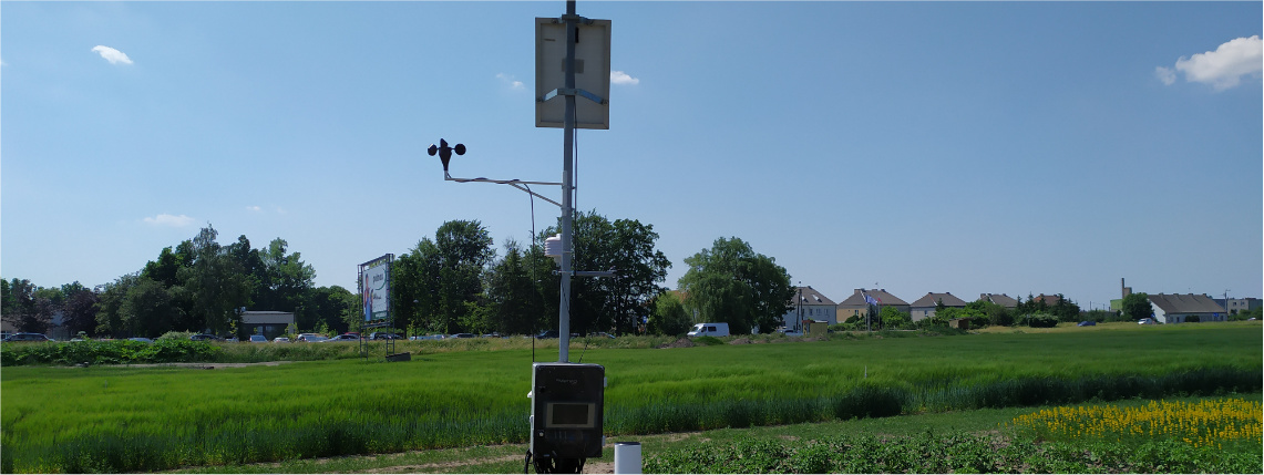 Platforma eDWIN dostarcza dane ze stacji meteorologicznych Na polu stoi stacja meteorologiczna. W tle zielona trawa, jasne niebo oraz zabudowania.