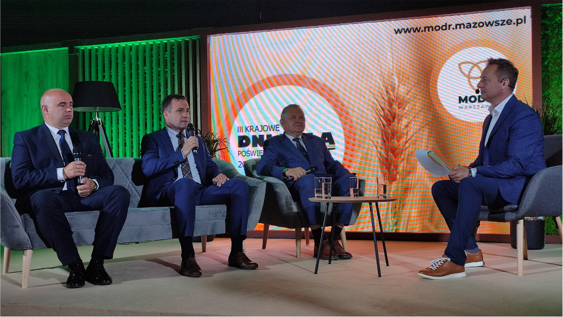 Dyrektor WODR Jacek Sommerfeld opowiadał o platformie eDWIN podczas panelu dyskusyjnego Wnętrze pomieszczenia, w którym jest studio telewizyjne. Czterej mężczyźni w garniturach siedzą na krzesłach i rozmawiają.