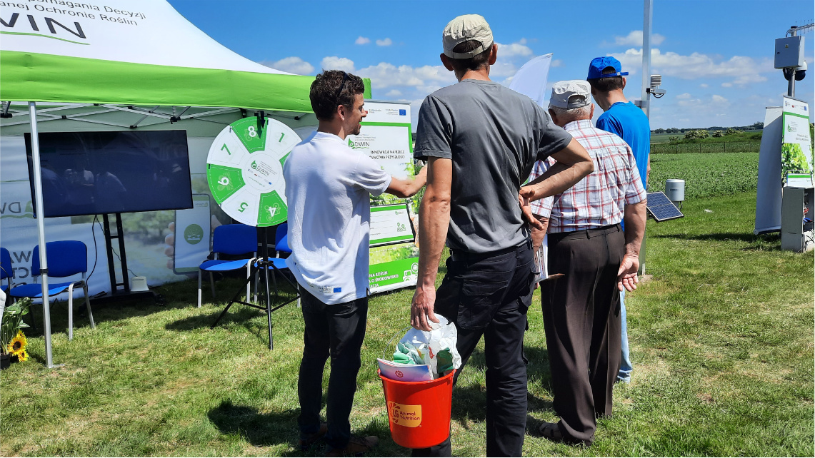 Doradcy rolniczy opowiadali o platformie eDWIN. Rolnicy stoją przy stoisku platformy eDWIN. Doradca rolniczy opowiada im o platformie.