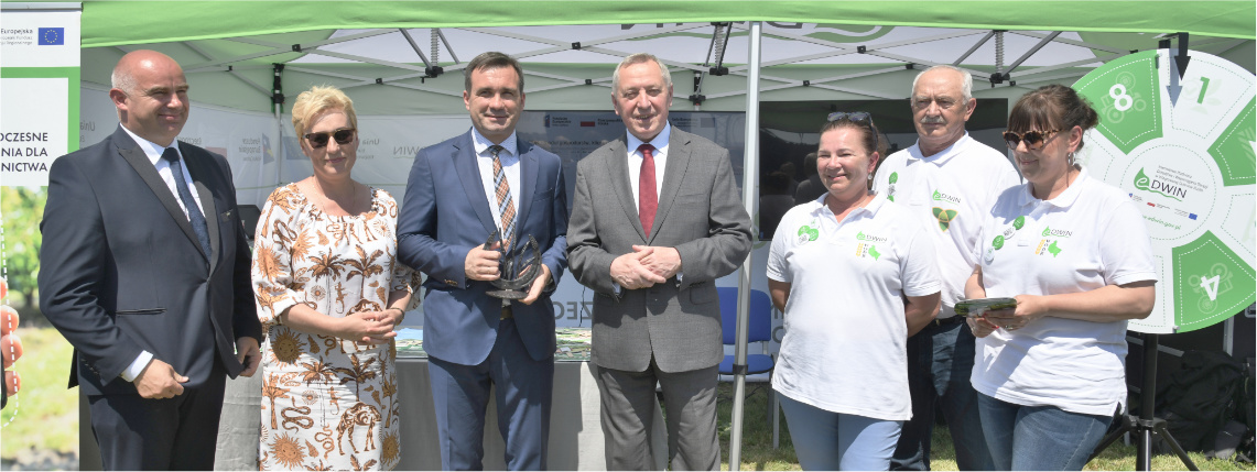 Stoisko platformy eDWIN odwiedził między innymi Henryk Kowalczyk, Minister Rolnictwa i Rozwoju Wsi Grupa kilku osób, w tym dyrektor WODR i minister rolnictwa, stoi przed namiotem eDWIN i pozuje do zdjęcia.