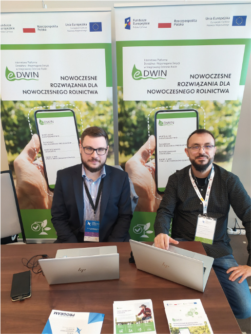 Informatycy WODR Adam Fojud (z lewej) i Maciej Zacharczuk (po prawej) byli obecni na Forum Inteligentnego Rozwoju prezentując projekt eDWIN Adam Fojud (po lewej) i Maciej Zacharczuk (po prawej) siedzą przy stole, na którym są laptopy i ulotki. W tle rollupy projektu eDWIN.