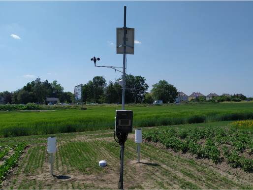 Stacje meteorologiczne są niezbędne w projekcie eDWIN Słoneczny dzień. Na polu stoi stacja meteorologiczna. W tle widać namiot eDWIN oraz flagi reklamowe.