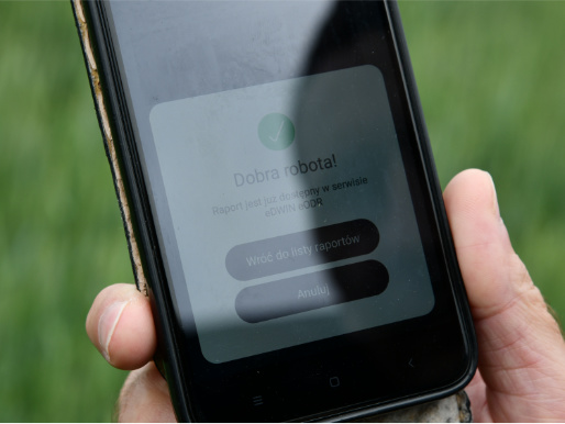 Doradcy rolniczy korzystają z aplikacji eDWIN na telefonach komórkowych Telefon komórkowy trzymany w rękach. Na wyświetlaczu telefonu niewyraźnie widoczne są informacje o eDWIN.
