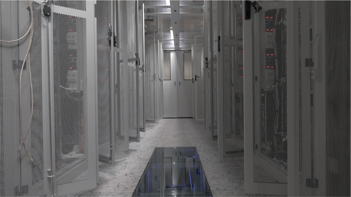 Centra danych odgrywają kluczową rolę w procesie cyfryzacji Wnętrze serwerowni PCSS. Po obu stronach wąskiego przejścia stoją szafy z serwerami. Drzwi do serwerów są otwarte.